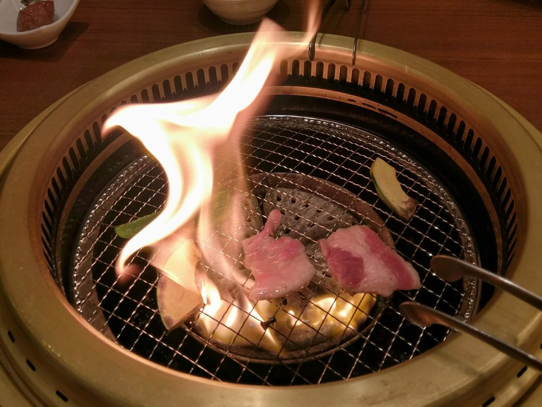 A flame flickers up from under a yakiniku grill and the meat cooking on it