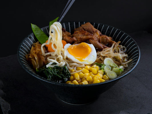 A bowl of ramen sits with beef, snap peas, corn and egg on top