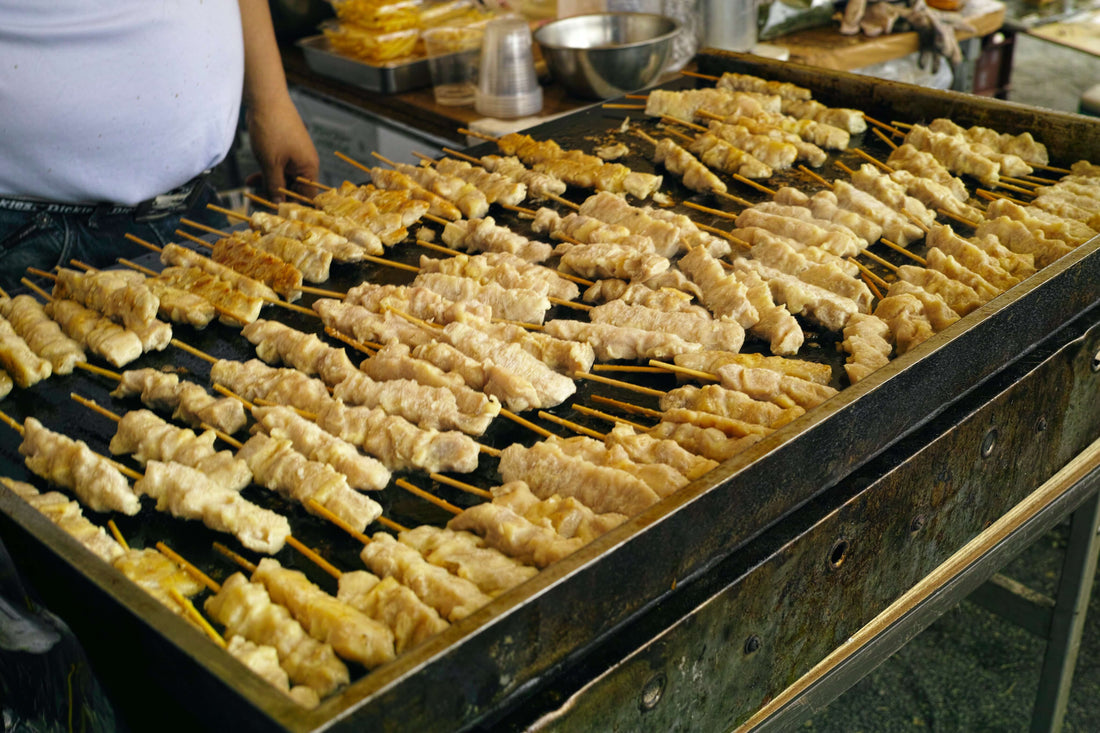 Many sticks of chicken sit on a yakitori grill with the chef standing behind it
